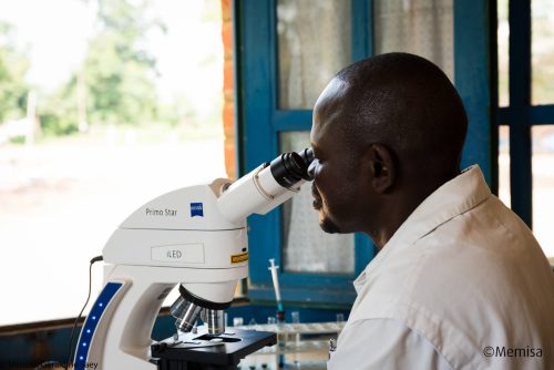 Un homme en blouse médicale regarde dans un microscope, RD Congo